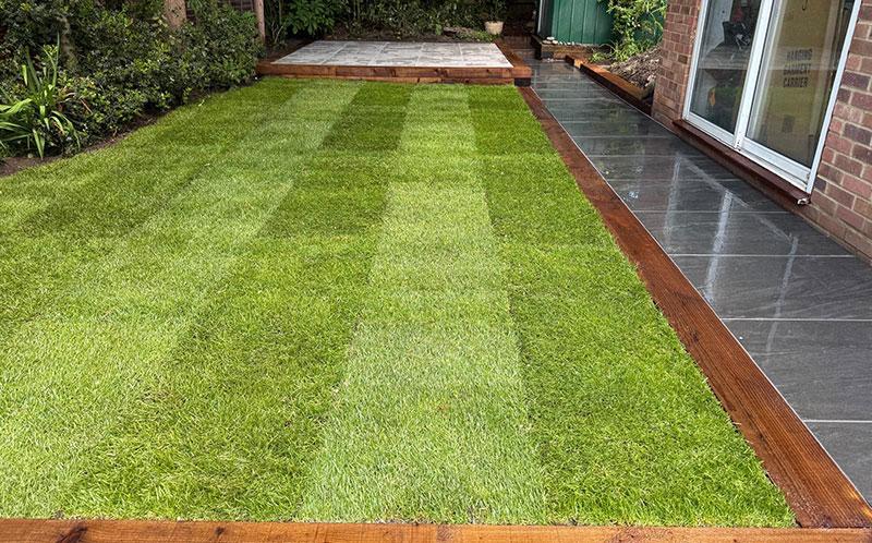 Fully installed new garden with freshly laid grass, sleeper edging and patio slabs